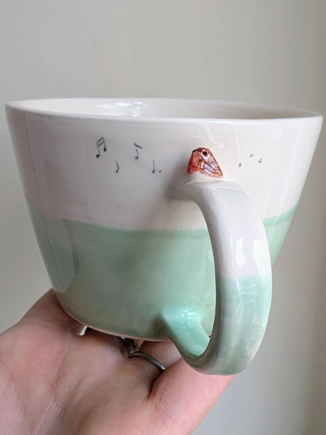ceramic bird cup in green and white with a tiny robin bird on the handle and musical notes and bird prints
