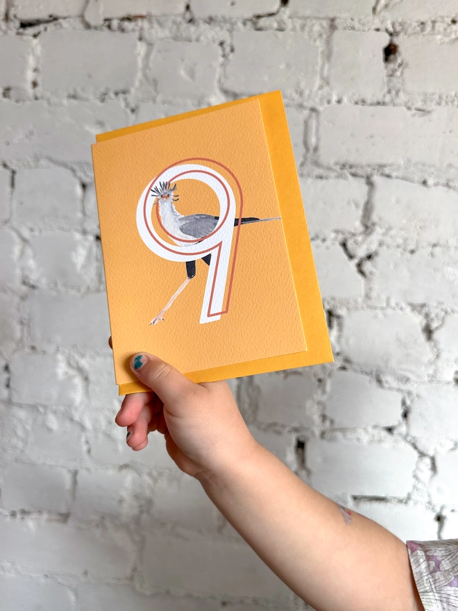 Bright yellow card with an illustration of a secretary bird and a big white number 9, with a yellow envelope