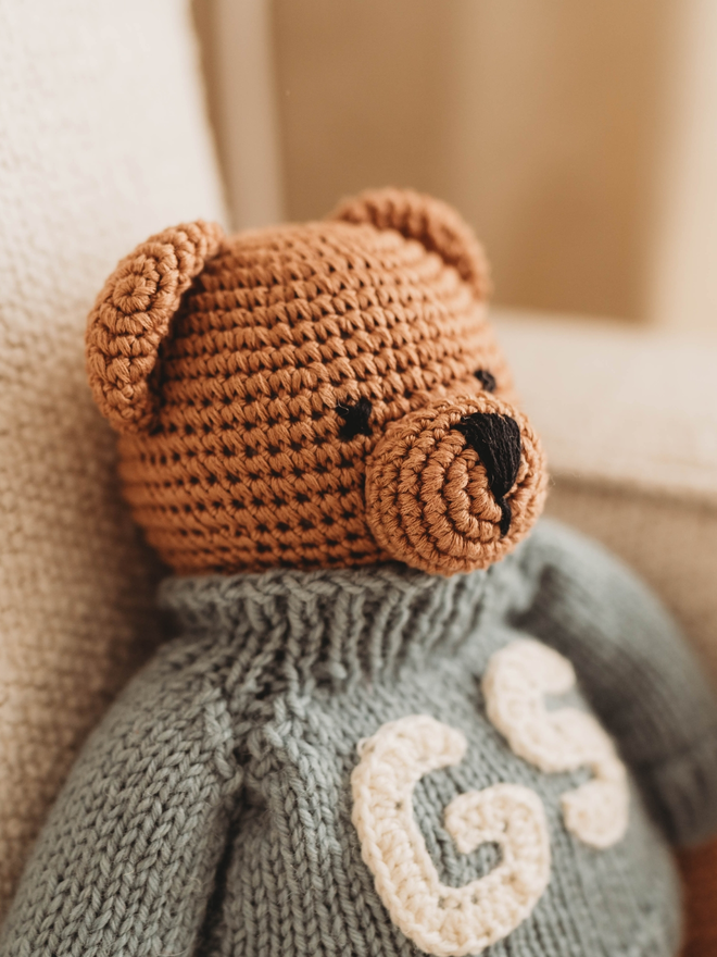 brown hand crochet teddy bear on beige sofa with hand knit personalised blue jumper