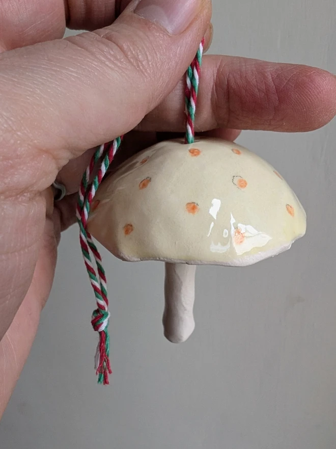 yellow and orange spotty ceramic mushroom hanging bell decoration held in a hand against a pale grey background