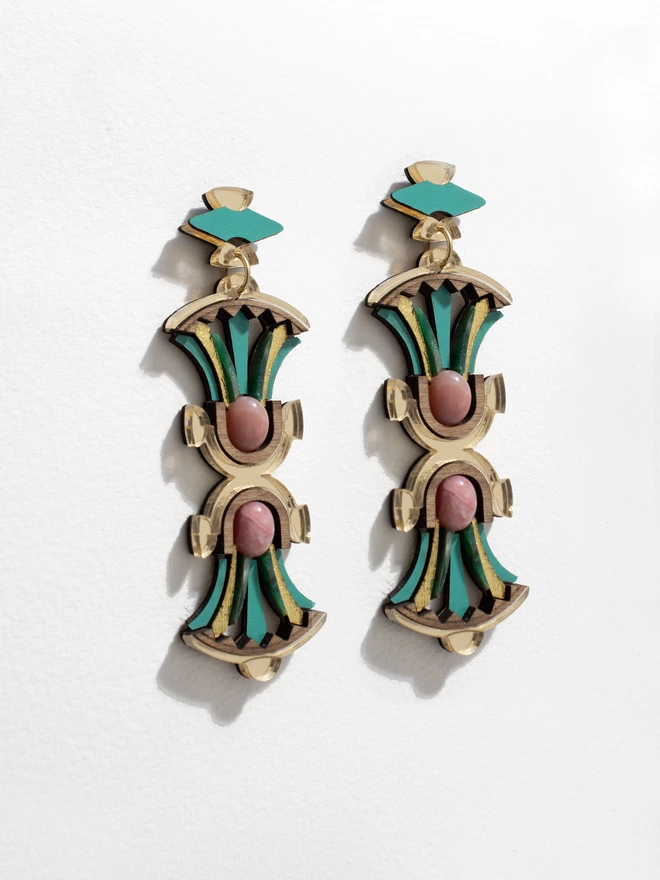 Pair of laser cut earrings with gold, green, and pink design on a white background