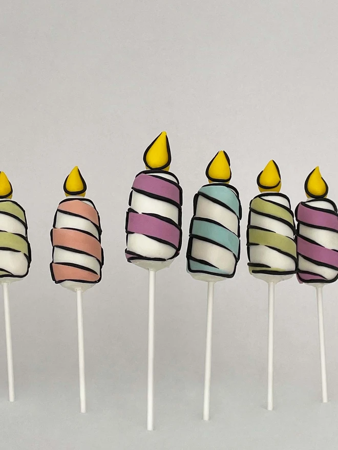 6 Cartoon Birthday Candle Cake Pops in various colours standing infront of a white background. 
