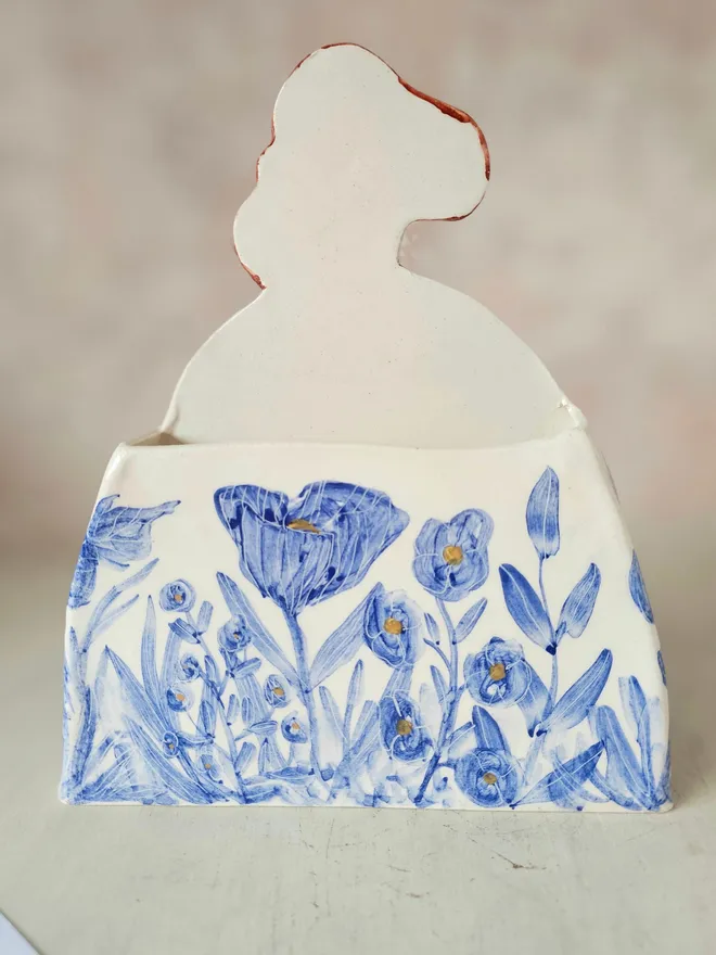a large vase shaped like a lady with red hair looking up with blue flowers painted on her dress, back view