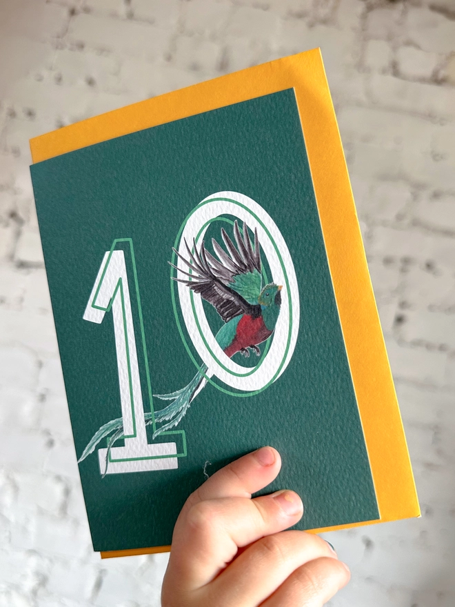 Deep green card featuring a big white number 10 and an illustration of a quetzal bird alongside a yellow envelope