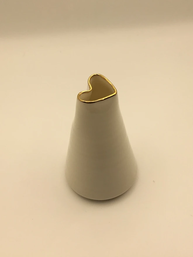 porcelain heart shaped bud vase. a white porcelain bud vase photographed on a white backdrop with a gold rim.