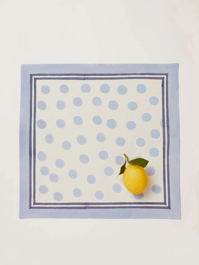 Single block printed cream napkin with a pale blue dot pattern and a lemon placed on the bottom left corner