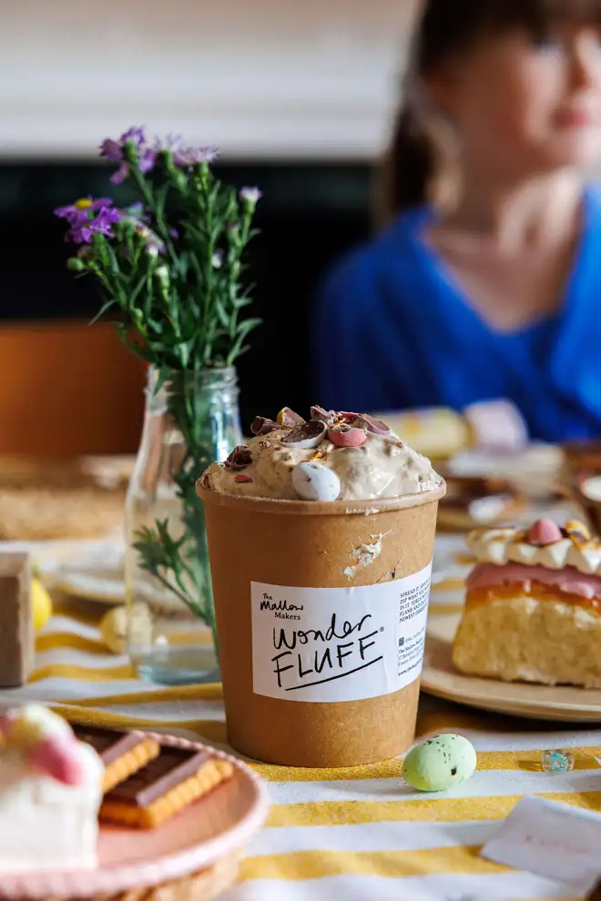 Mini Eggs Wonder Fluff tub opened with crushed mini eggs on a table with easter decorations and a child in the background