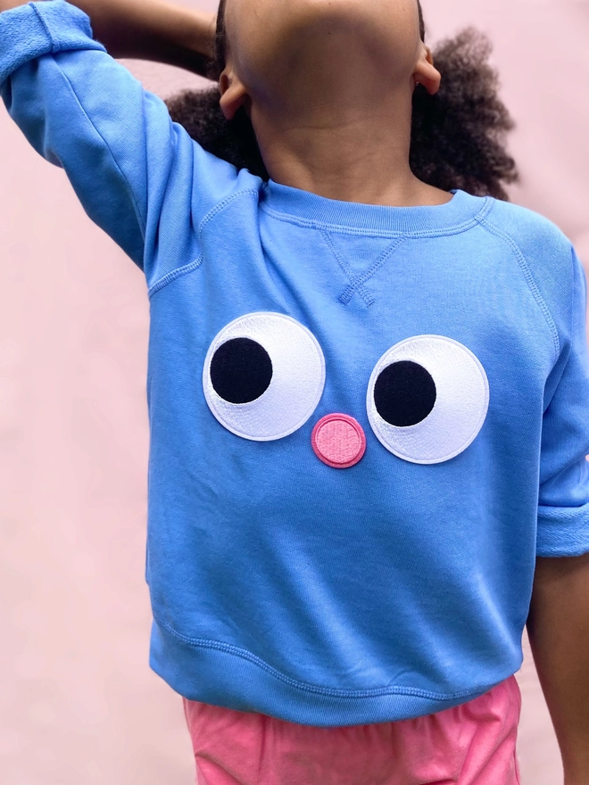 A girl wearing a blue jumper with DIY eyes & nose iron on patches 