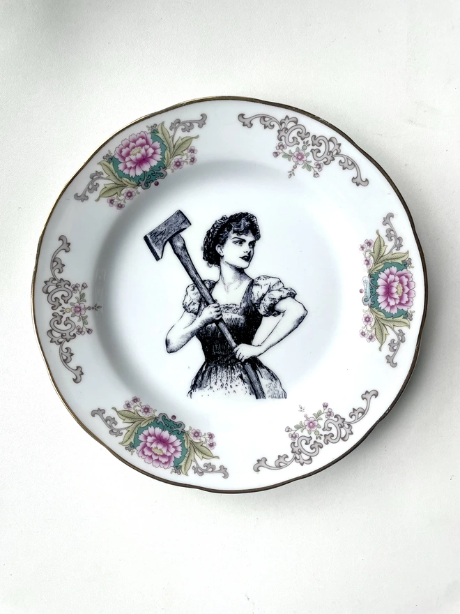 a vintage plate with a really ornate pretty border has a vintage black and white illustration of a beautiful girl in peasant clothes wielding an axe