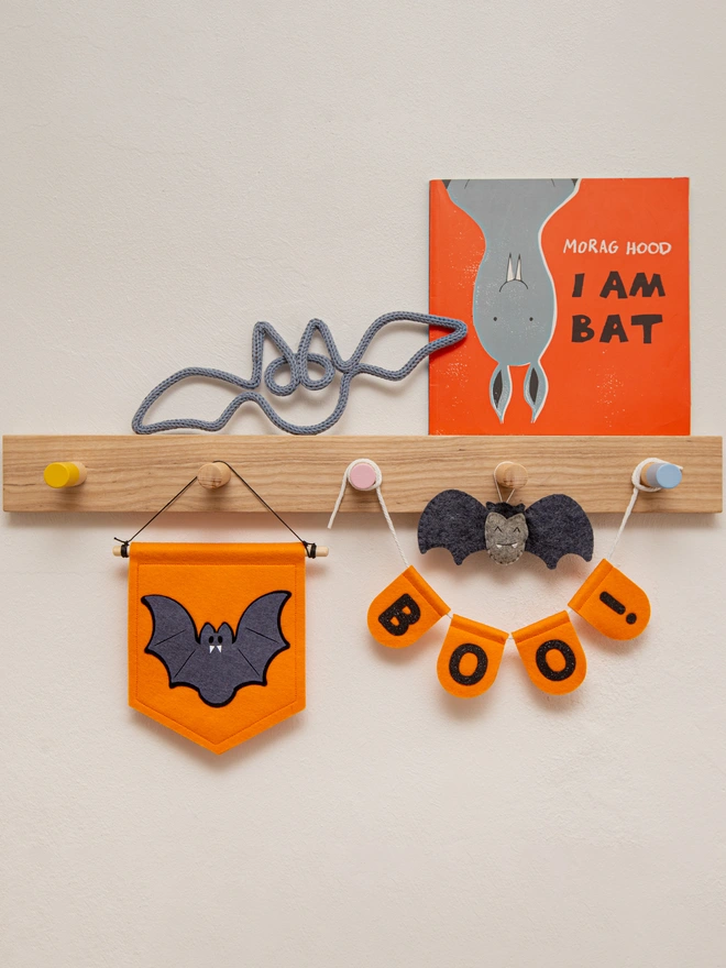 Cute halloween bat banner made from felt. The banner is orange with a dark grey and black bat. Next to the bat is a small orange scalloped bunting that says 'BOO!' in black glitter