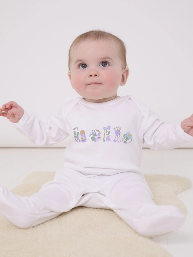  a new baby wearing a white cotton romper with hello sewn onto it in a floral print
