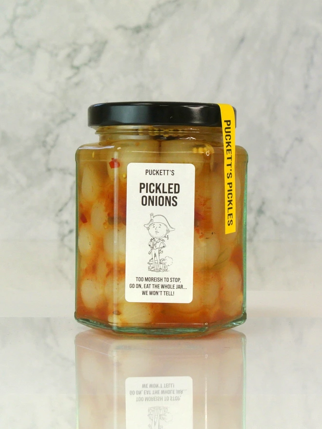 british pickled onions. a jar of pickled onions photographed against a marble background.