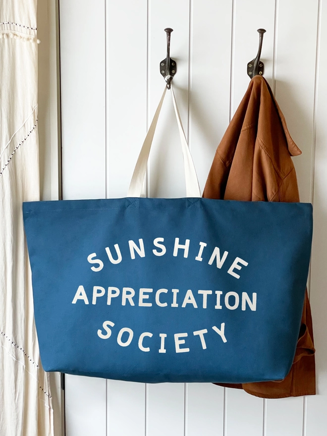 Blue oversized sunshine appreciation society bag hanging on a hook