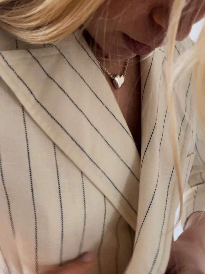 a model wearing a silver heart pendant with a white linen pinstripe suit jacket