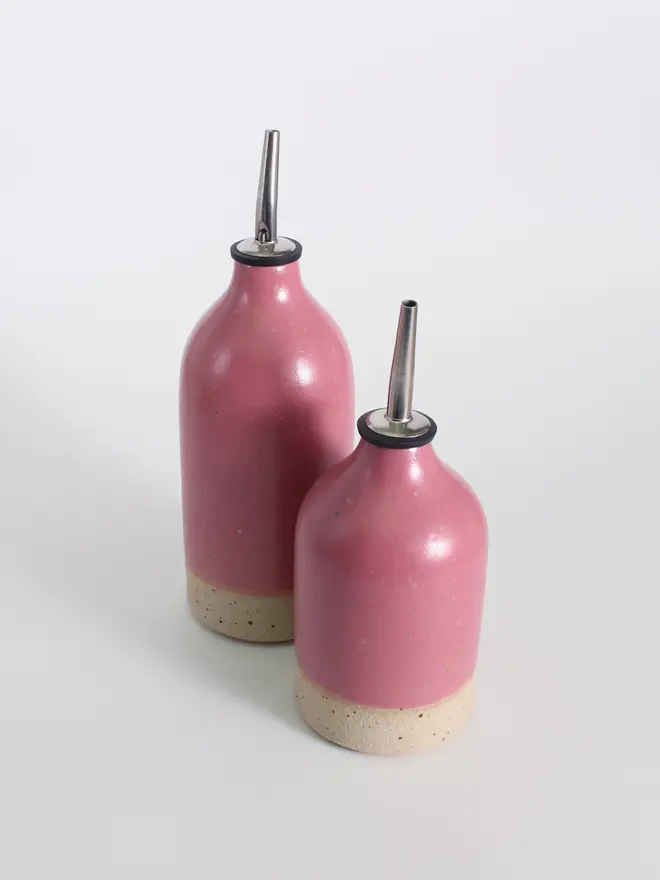 Small and large ceramic oil pourers in fuchsia against a white background