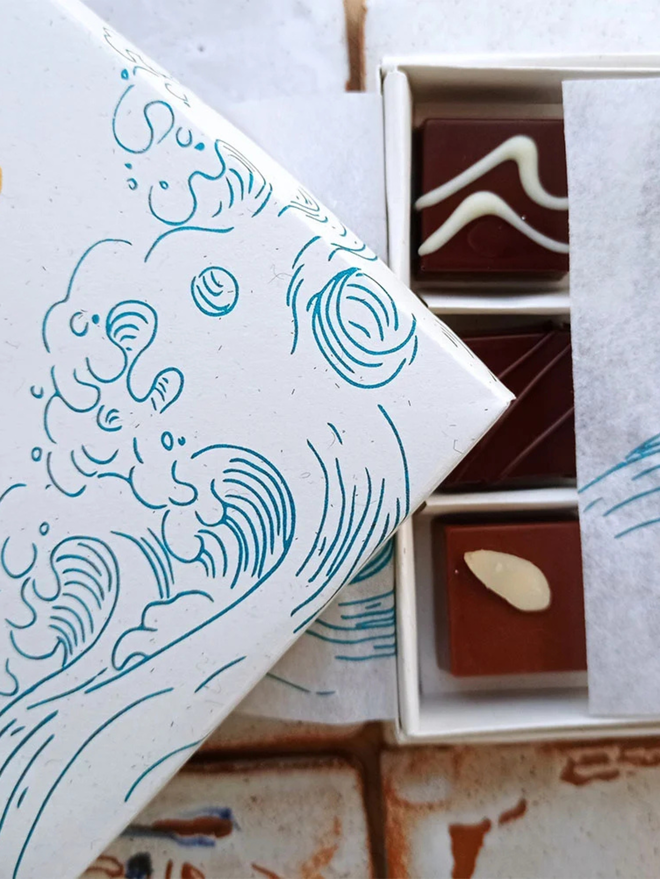 'walk to walpole' chocolate selection box. a white cardboard box with a blue illustrated wav, showing a selection of three types of chocolate inside.