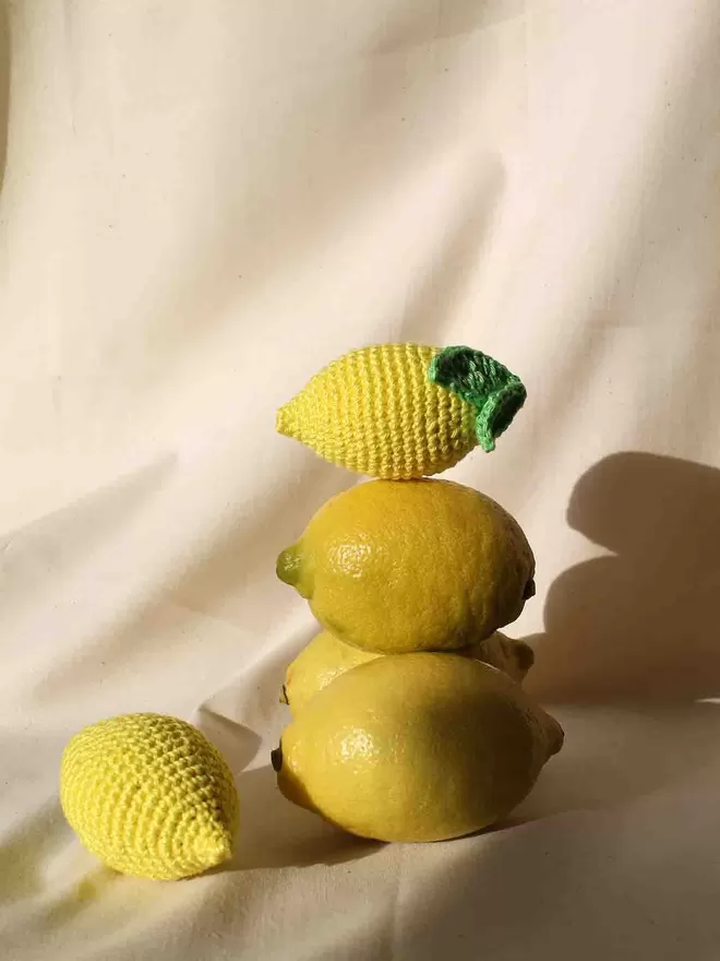 Stack of three lemons with one crochet lemon on top and another crochet lemon to the side.