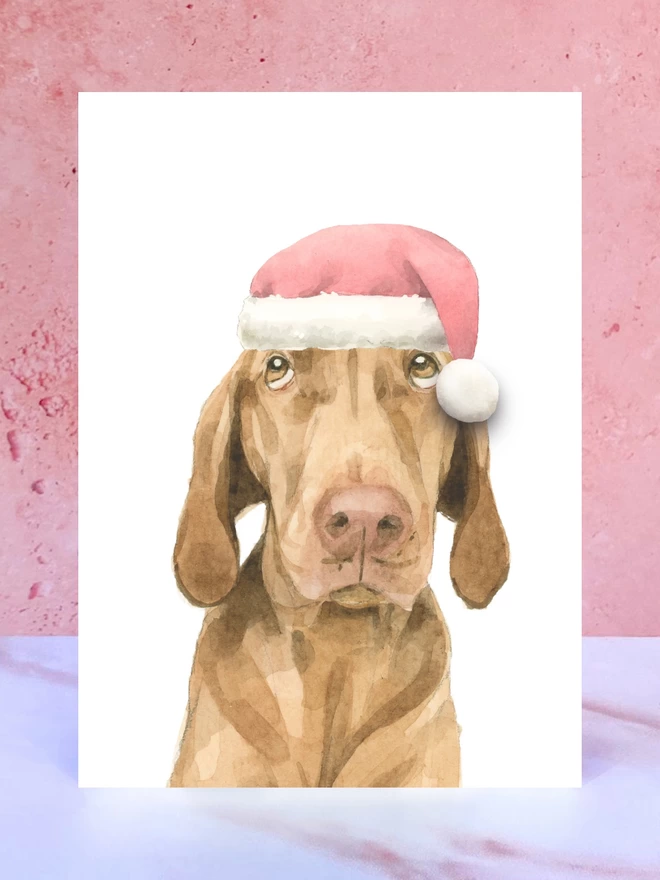 A Christmas card featuring a hand painted design of a vizsla, stood upright on a marble surface. 