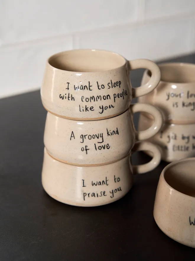 three cream ceramic mugs stacked on top of one another with various phrases 