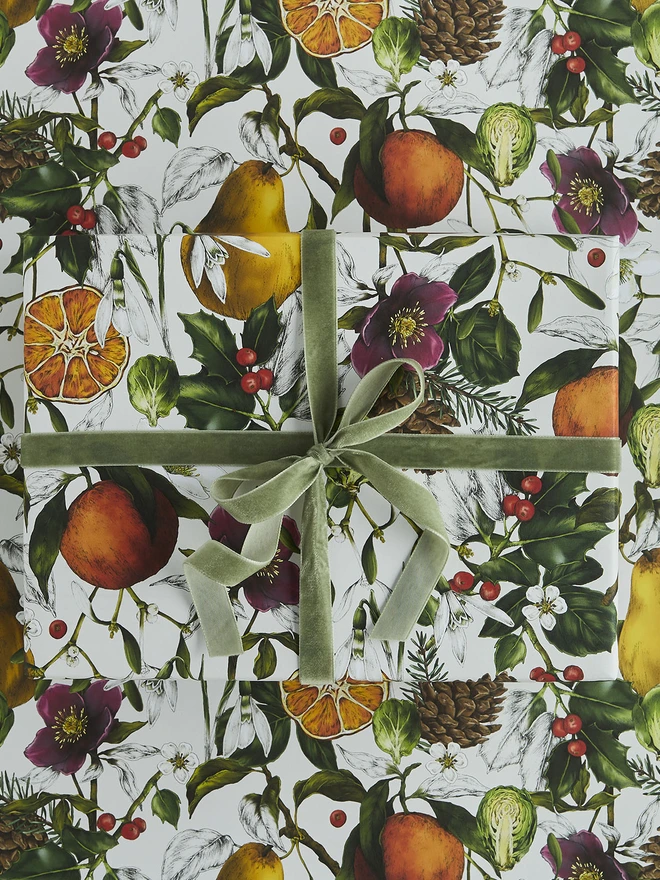 A busy ivory based christmas wrap with festive elements like clementines, holly and hellebores