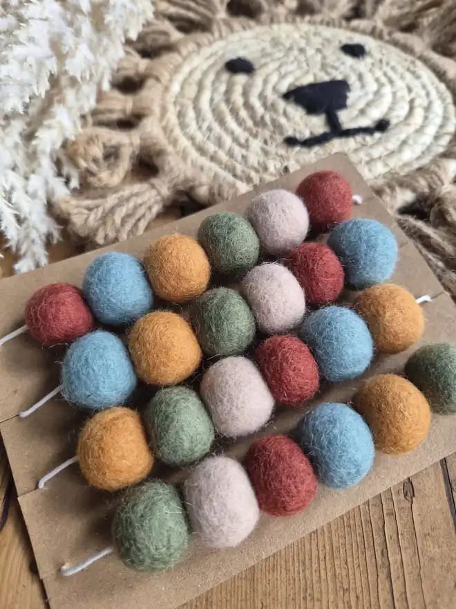 Boho garland made with 2cm felt ball pom poms. Displayed and wrapped around a brown kraft card.