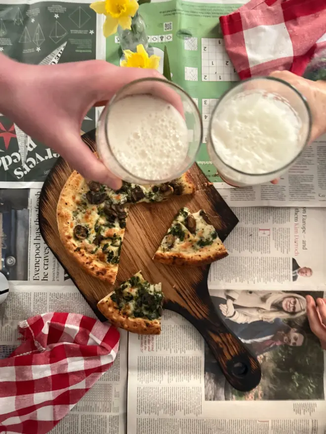 Cheers beers over pizza board styled on newspaper with daffodils beer pizza  and red gingham napkin