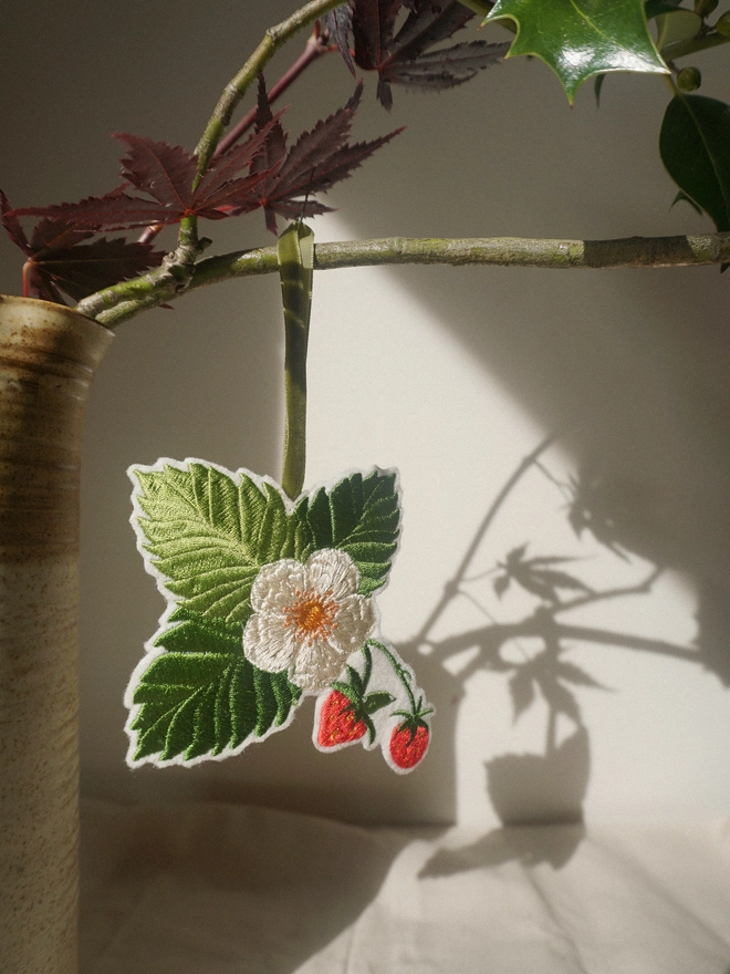 Embroidered strawberry and blossom hanging decoration with green velvet ribbon, styled with seasonal foliage.