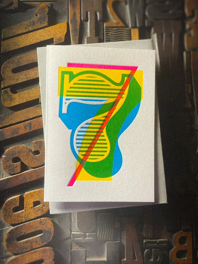 Handmade letterpress 7th birthday card featuring bold overlapping numerals printed in vibrant fluorescent cyan, magenta and yellow inks. Each card is individually hand printed using traditional letterpress techniques on luxury paper stock, creating a beautifully tactile finish with a deep impression and rich layered colours inspired by the CMYK printing process. Printed on a traditional letterpress from 1915. A wonderful artisan printed birthday card.