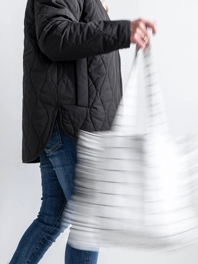 Lady in black jacket swinging a white tote bag