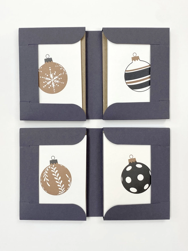 Two open gift boxes showing snowflake, four stripe, leaf and spot designs in gold and black on small cards