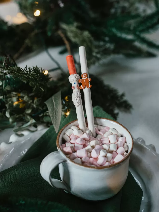 Ceramic Gingerbread Men Drinking Straw seen with a santa straw in a hot chocolate with marshmallows.