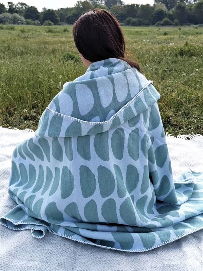 Organic Cotton Throw, a woman sitting with a throw draped on her outside. 