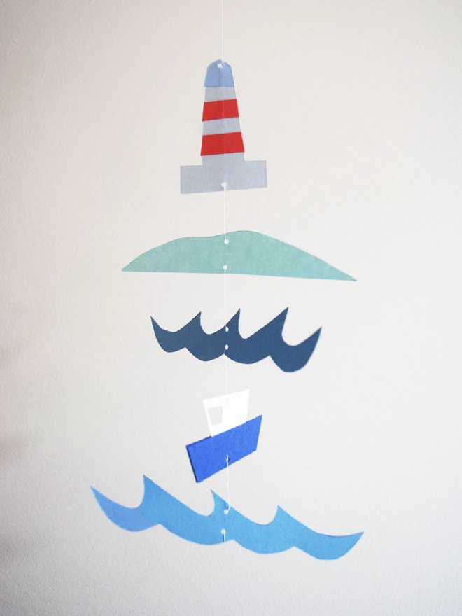 A paper mobile with a lighthouse, landscape, sea and boat