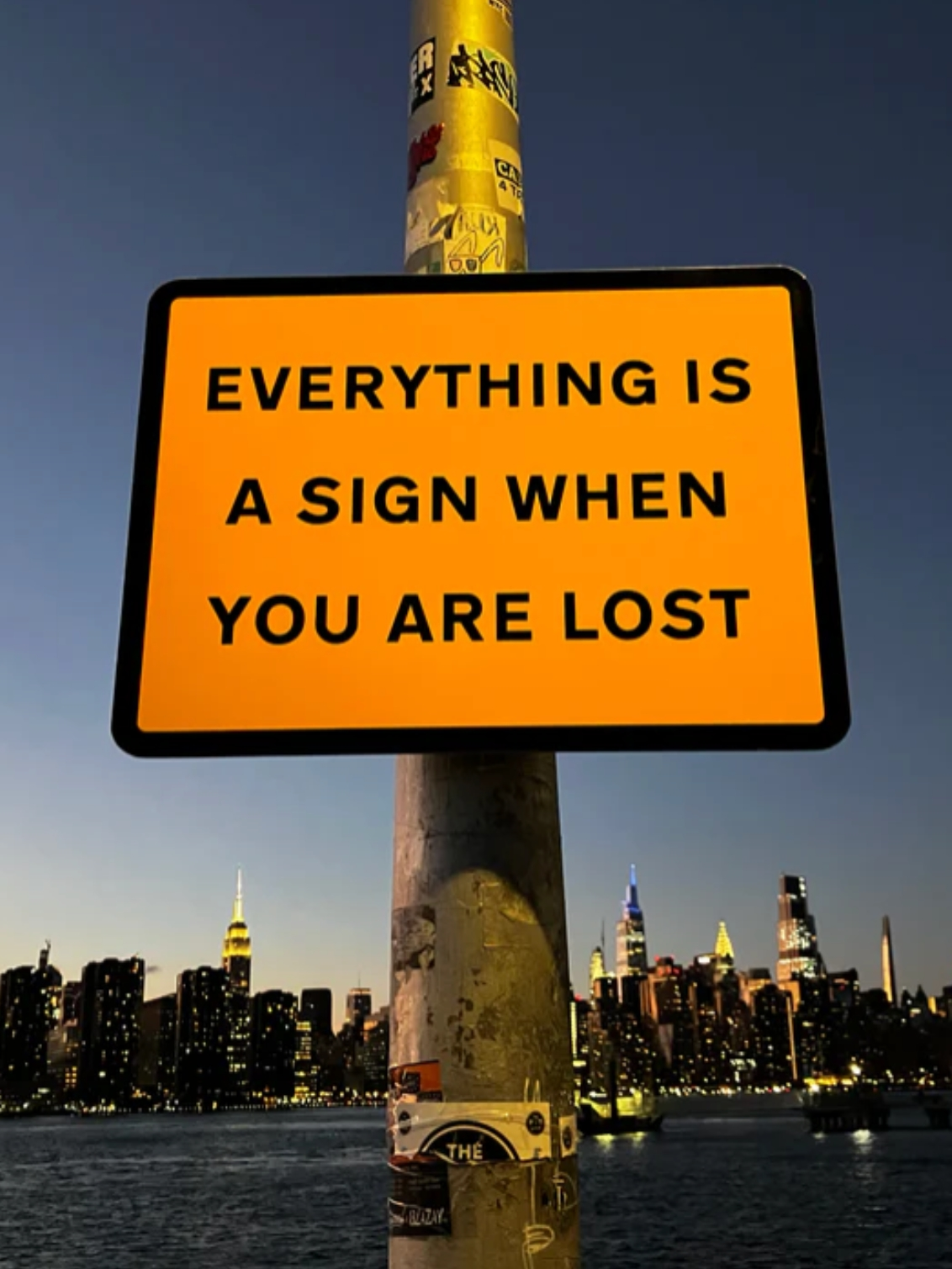 It’s a Sign. A sign on a lamppost with a cityscape behind.