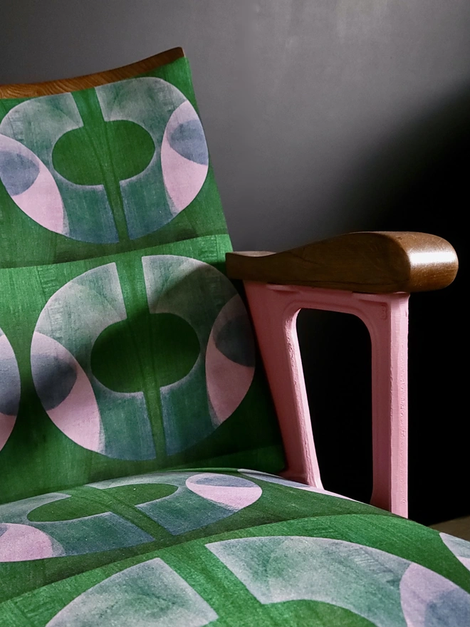 Close up of cinema seat with pink legs, green and pink velvet on a black wall.