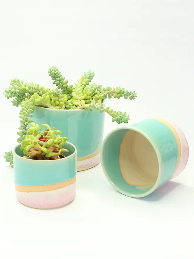 The large, medium and small shoreline plant pots on a white background. The medium pant pot is on its side showing the raw stoneware interior.