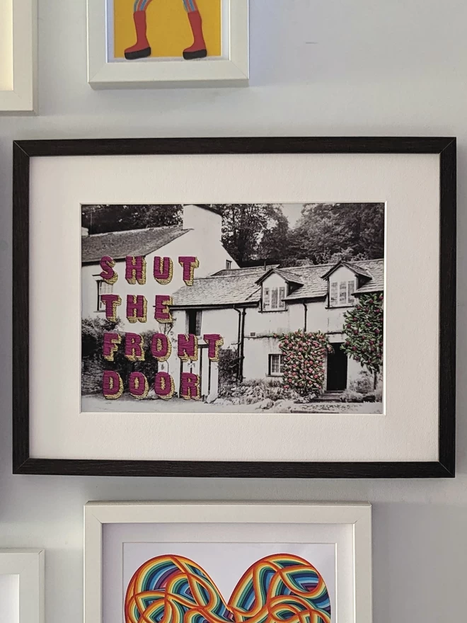 Print of Shut the front door embroidered on B&W cottage in frame on wall