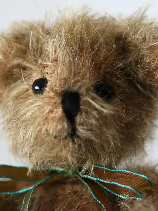 Small handmade brown teddy bear with a ribbon bow sitting against a plain background.