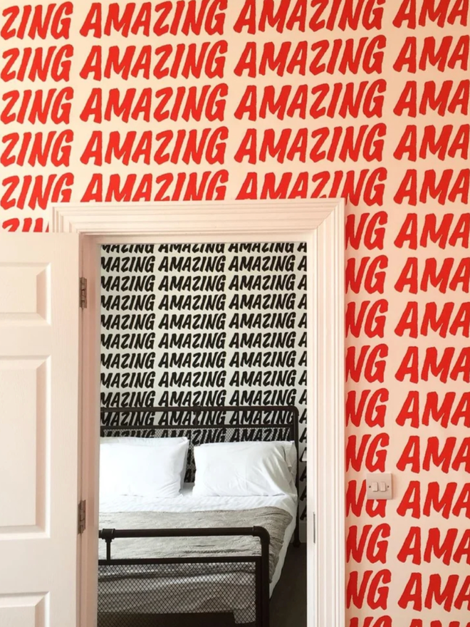 Amazing Wallpaper. An open door surrounded by wallpaper which reads AMAZING in a red, all caps font, repeated. Through the door there is a bedroom with the black variant visible.