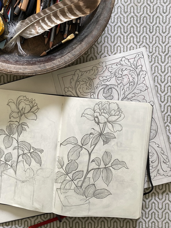 Sketchbook with pencil drawings of roses and a wooden bowl filled with drawing equipment