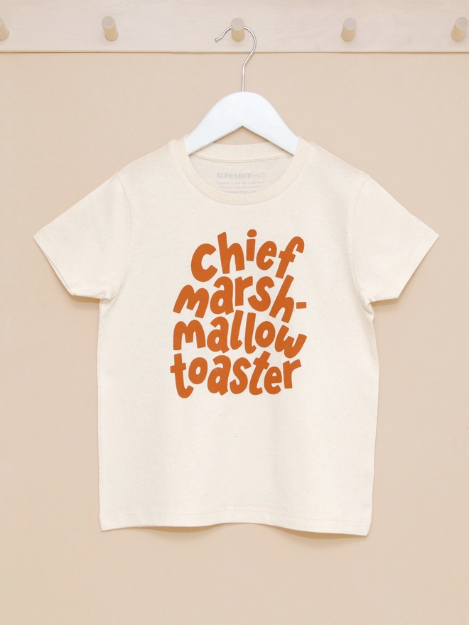chief marshmallow toaster organic cotton kid's t-shirt handing from a wooden hook