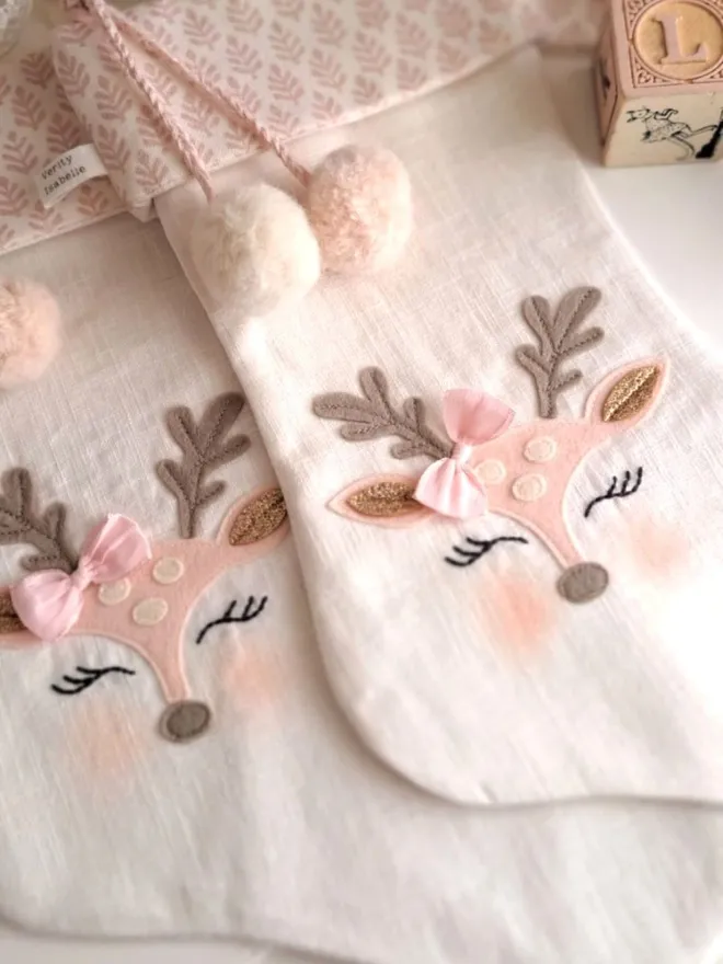 Two baby Bambi Christmas stockings, with cute faces, embroidered sleeping eyes, rosy cheeks and pink bow near the antlers. 