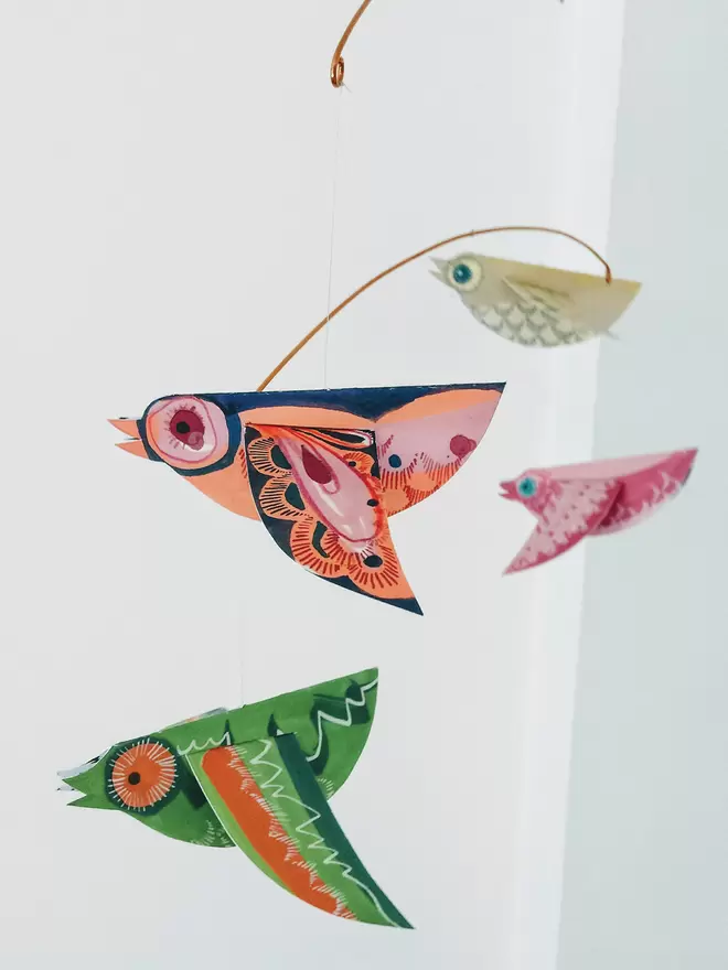 Colourful Paper Birds Mobile, with green, orange and pink patterned birds hanging against a white wall.  