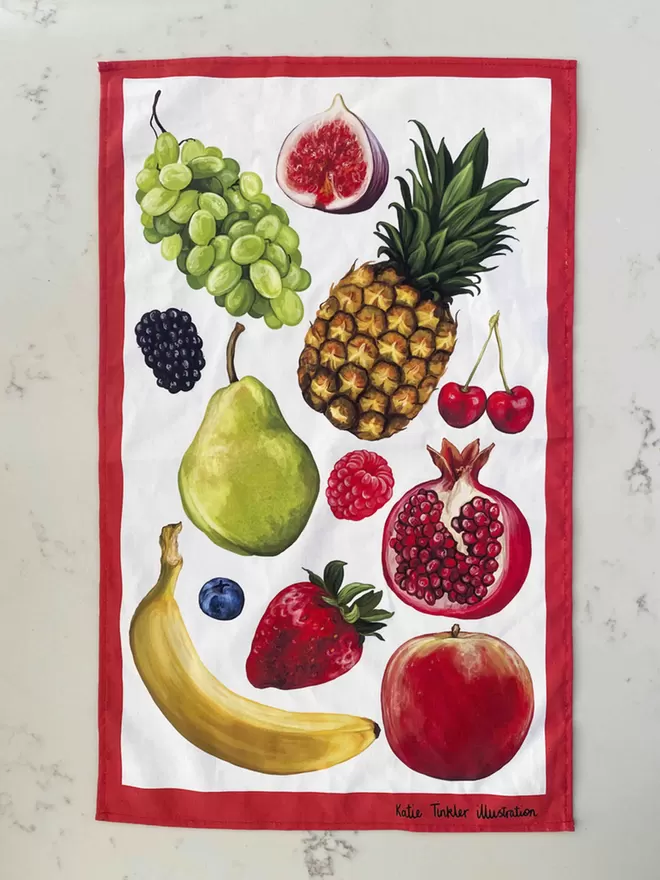A fruit themed tea towel laid out on a marble table