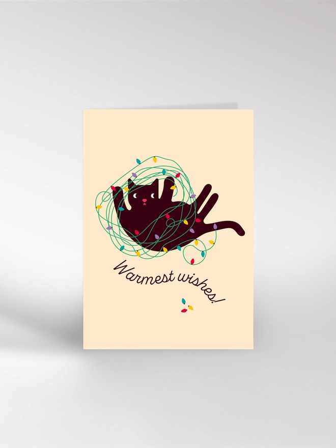 Illustrated Christmas card of a black cat tangled up in colourful fairy lights