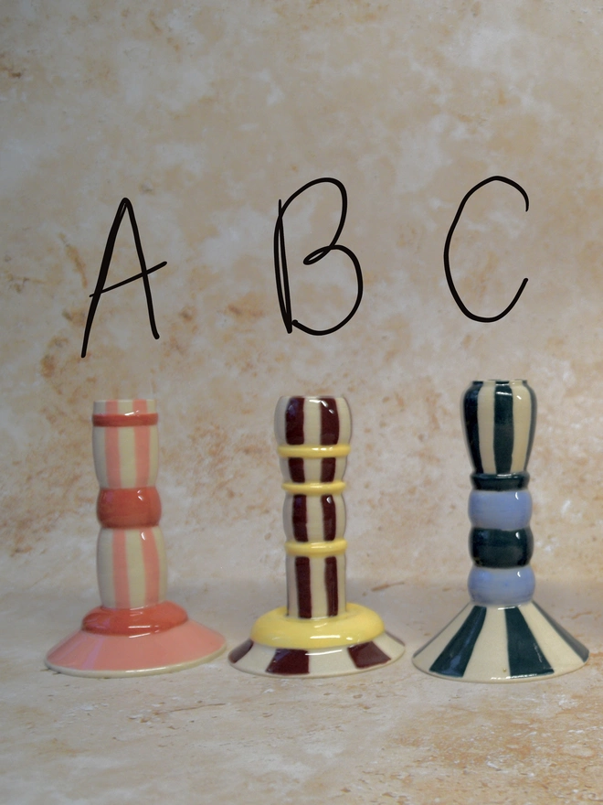 Handmade striped ceramic candlestick holders in three colour options, labelled A, B and C, featuring pink, yellow-burgundy and blue striped designs.