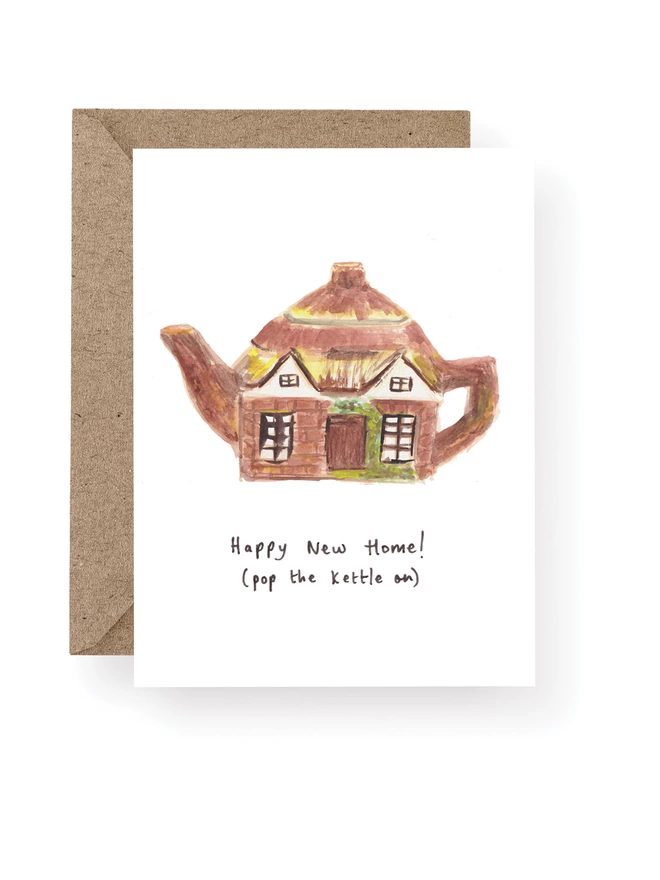 Happy New Home Cottage Teapot Card, Card Has a White Base With Hand Painted Vintage China Cottage Teapot.  Sitting On A Recycled Brown Kraft Envelope.  There Is Black Handwritten Text Underneath The Teapot Which Reads ‘Happy New Home! (Pop the kettle on)’