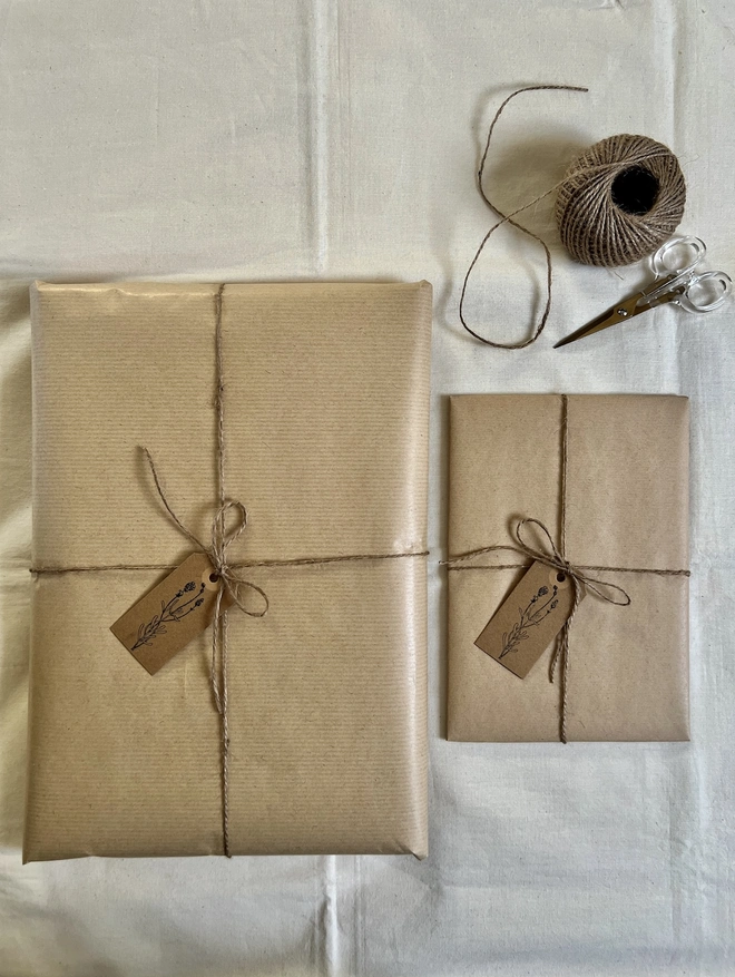 two different size artworks gift wrapped in brown paper with a hand stamped flower tag and brown string 