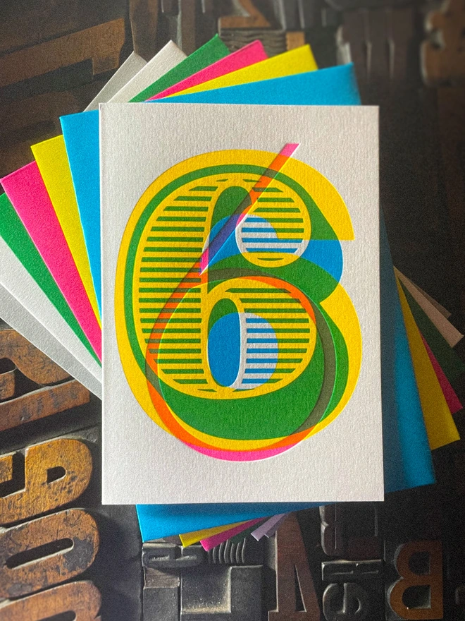 Handmade letterpress 6th birthday card featuring bold overlapping numerals printed in vibrant fluorescent cyan, magenta and yellow inks. Each card is individually hand printed using traditional letterpress techniques on luxury paper stock, creating a beautifully tactile finish with a deep impression and rich layered colours inspired by the CMYK printing process. Printed on a traditional letterpress from 1915.