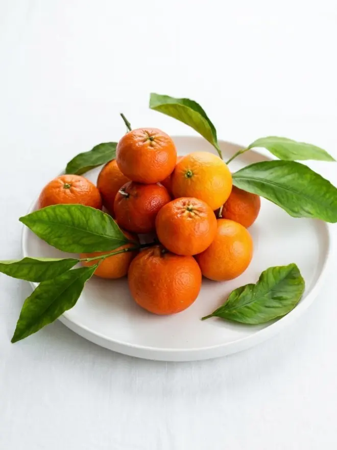 Christmas Satsuma Candle. a stack of candles shaped like satsuma oranges on a white round plate.